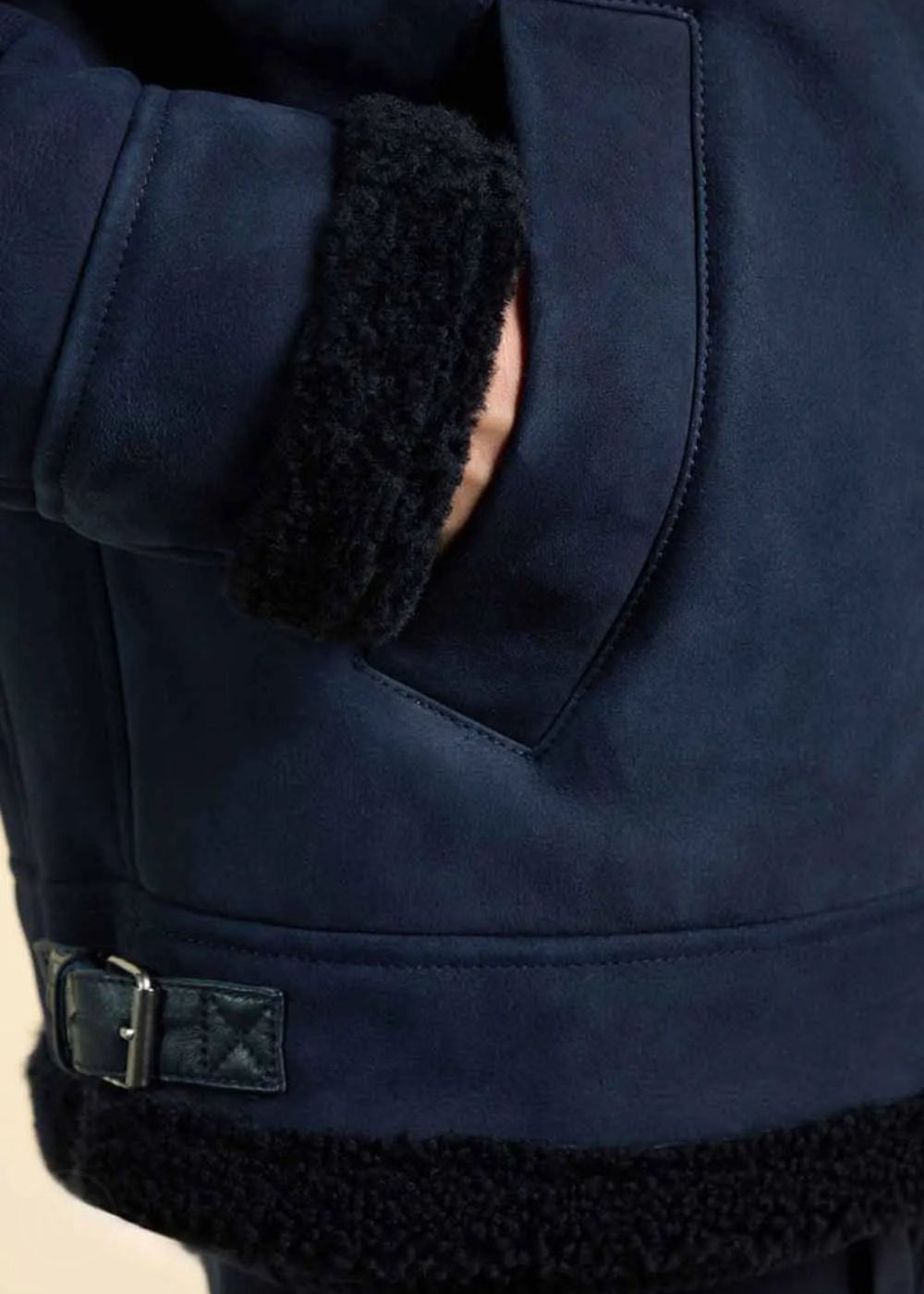 Close-up of a navy blue suede jacket with black fur trim on cuffs and waistband.