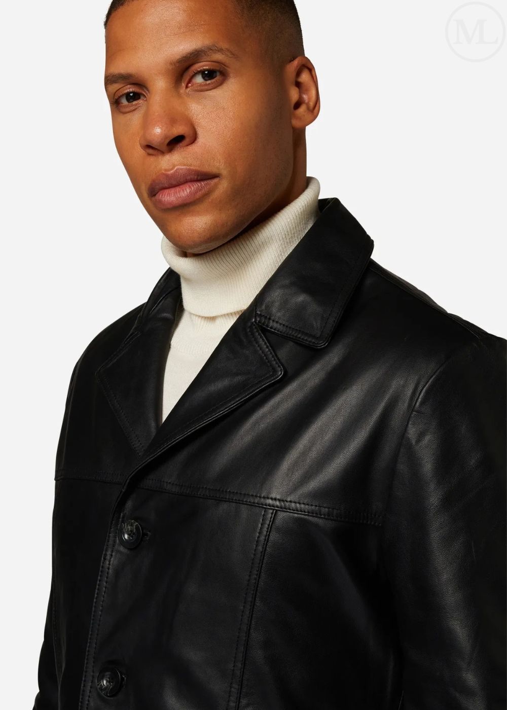 Man wearing a black leather trench coat over a white turtleneck on a plain background