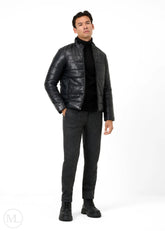 Man wearing a black leather puffer jacket, black turtleneck, gray pants, and black shoes on a white background