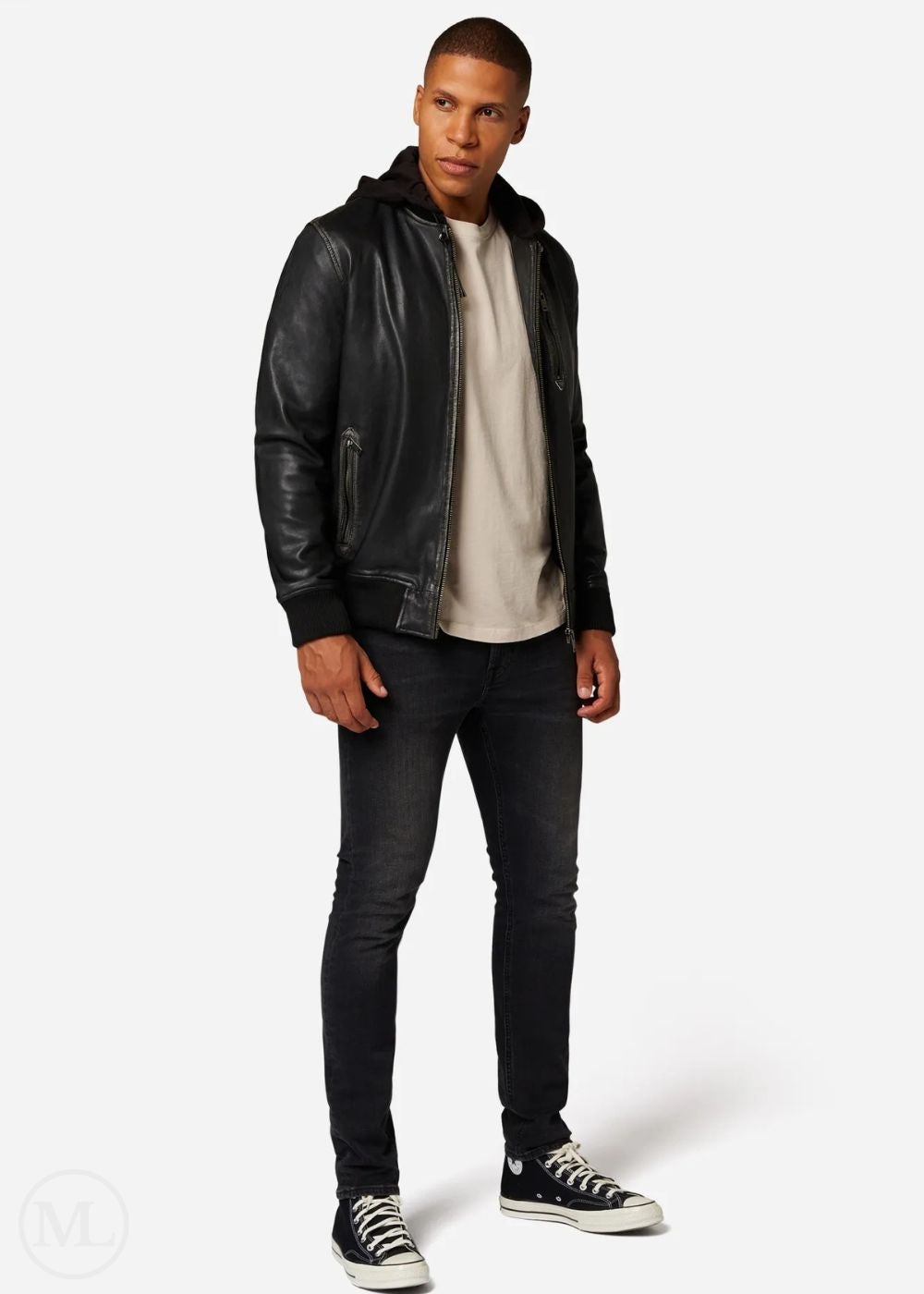 Man wearing a black leather hooded bomber jacket, white shirt, black jeans, and black sneakers on a white background