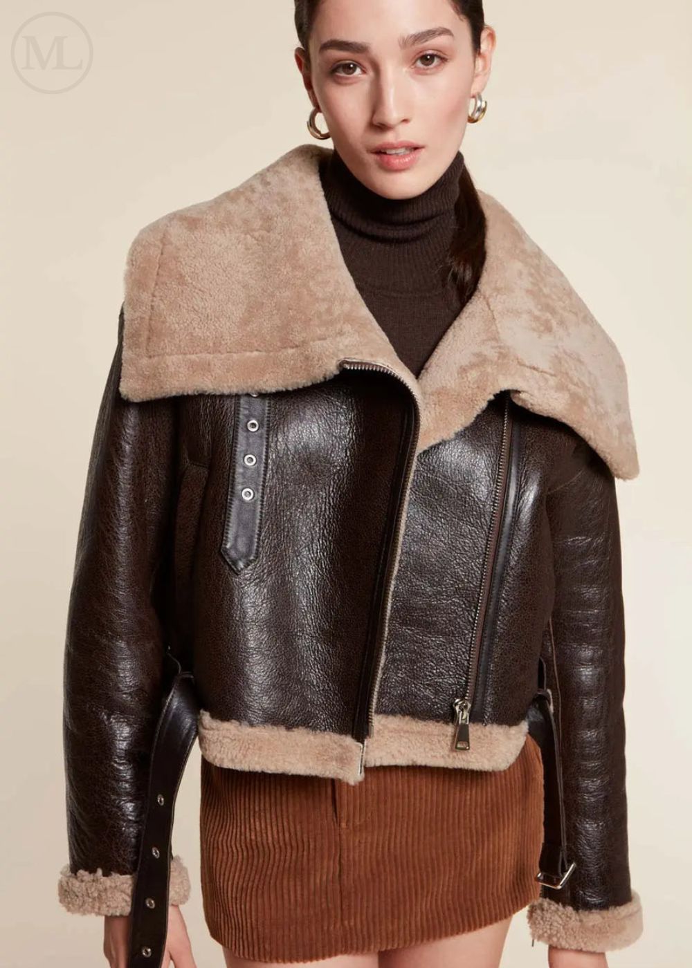 Woman wearing a dark brown aviator jacket with fur collar on a beige background