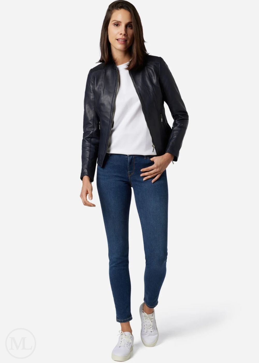 Woman wearing a blue leather jacket, white shirt, blue jeans, and white sneakers on a white background