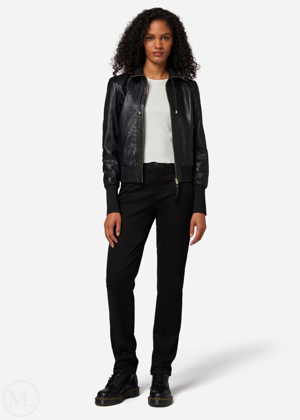 Woman wearing a black leather bomber jacket, white shirt, and black pants on a white background
