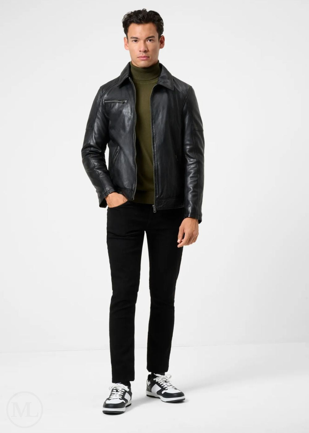 Man wearing a black leather racer jacket, green shirt, black pants, and black and white sneakers on a white background