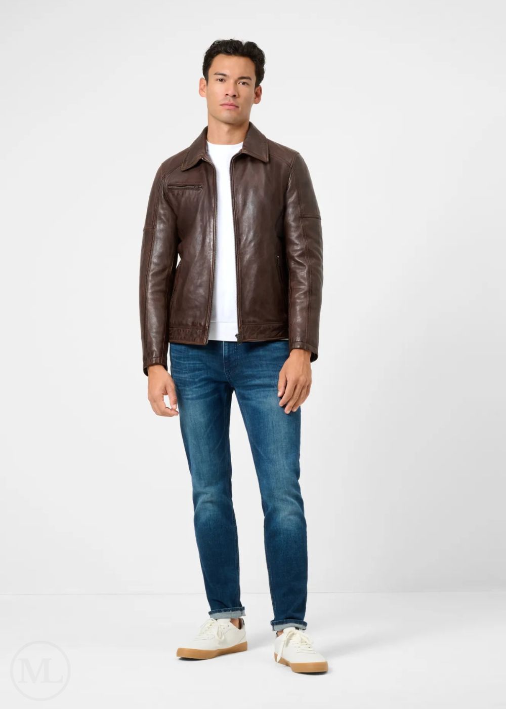 Man wearing a dark brown leather racer jacket, white shirt, blue jeans, and white sneakers on a white background