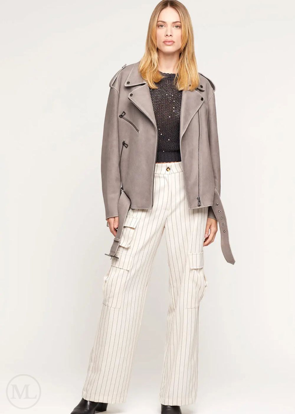 Femme portant une veste de motard surdimensionnée en cuir nubuck gris avec ceinture à la taille et un pantalon à fines rayures blanches sur fond blanc