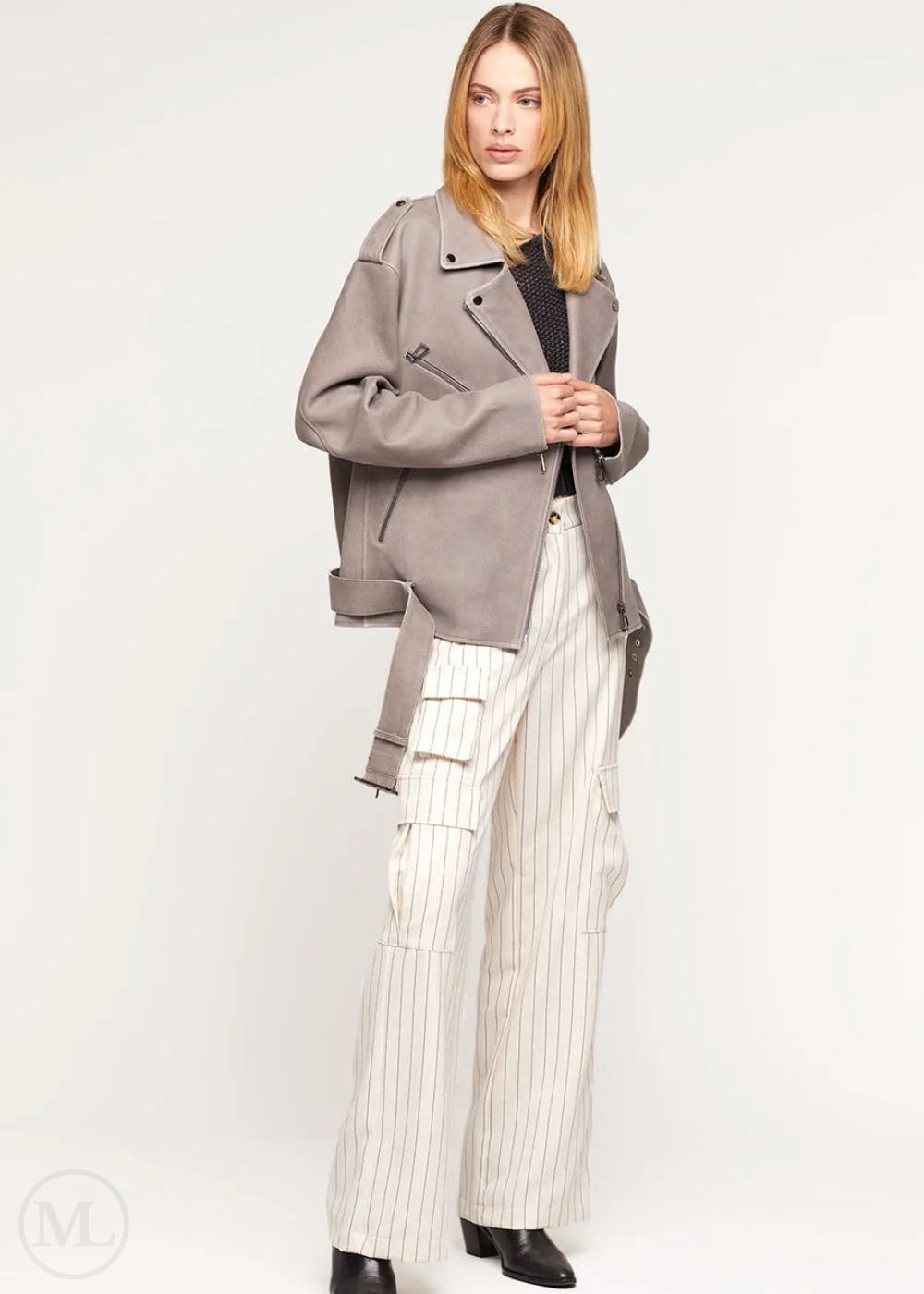 Femme portant une veste de motard surdimensionnée en cuir nubuck gris avec ceinture à la taille et un pantalon à rayures blanches sur fond blanc