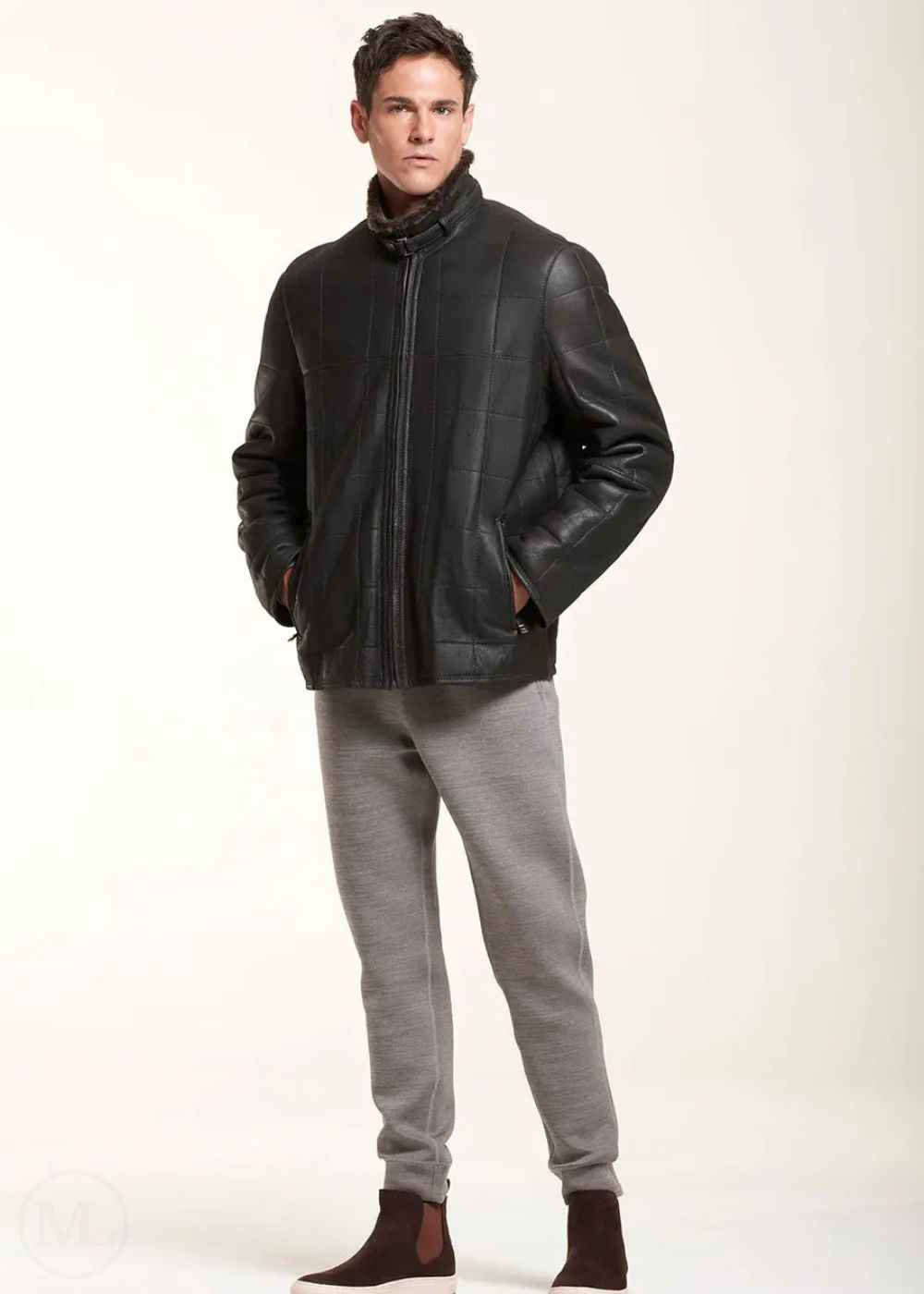 Man wearing a black leather jacket and gray pants on a white background