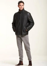 Man wearing a black leather jacket and gray pants on a white background