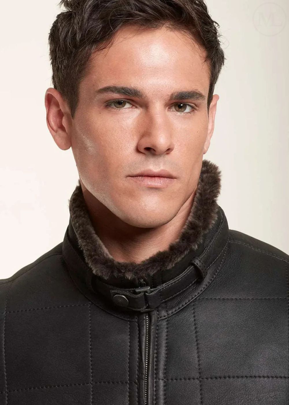 Man wearing a black leather jacket with a fur-lined collar against a plain background