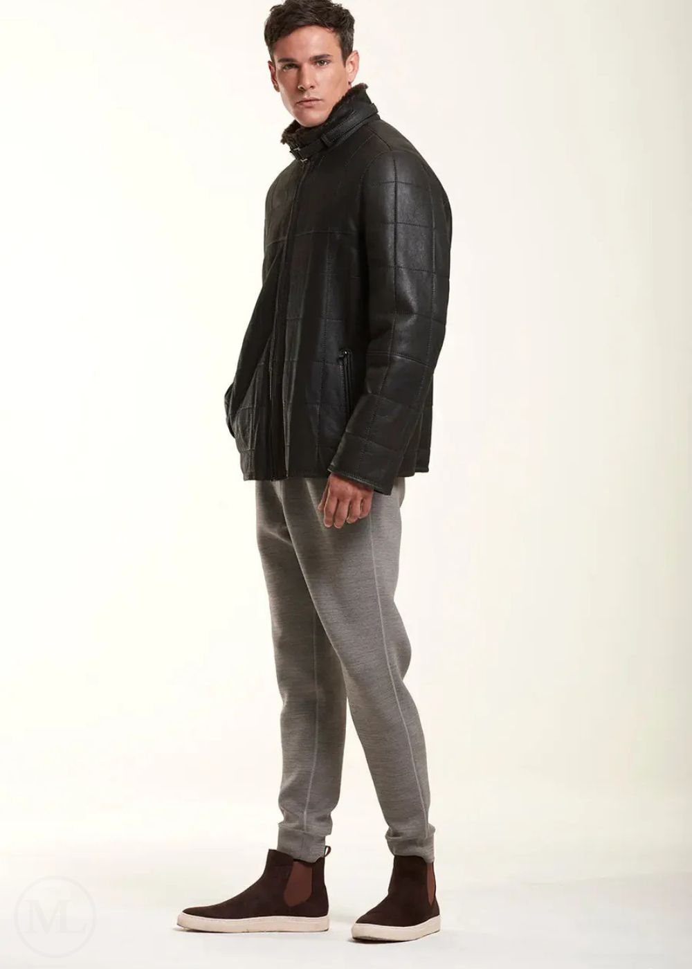 Man wearing a black leather jacket and gray pants on a white background