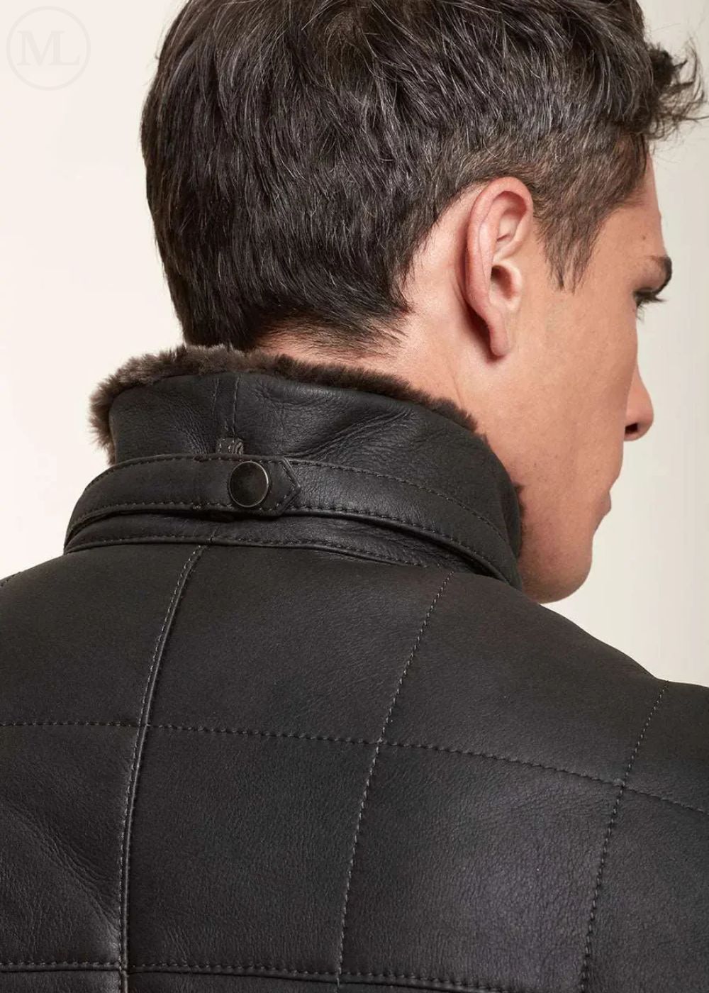 Man wearing a black leather jacket with fur collar on a neutral background