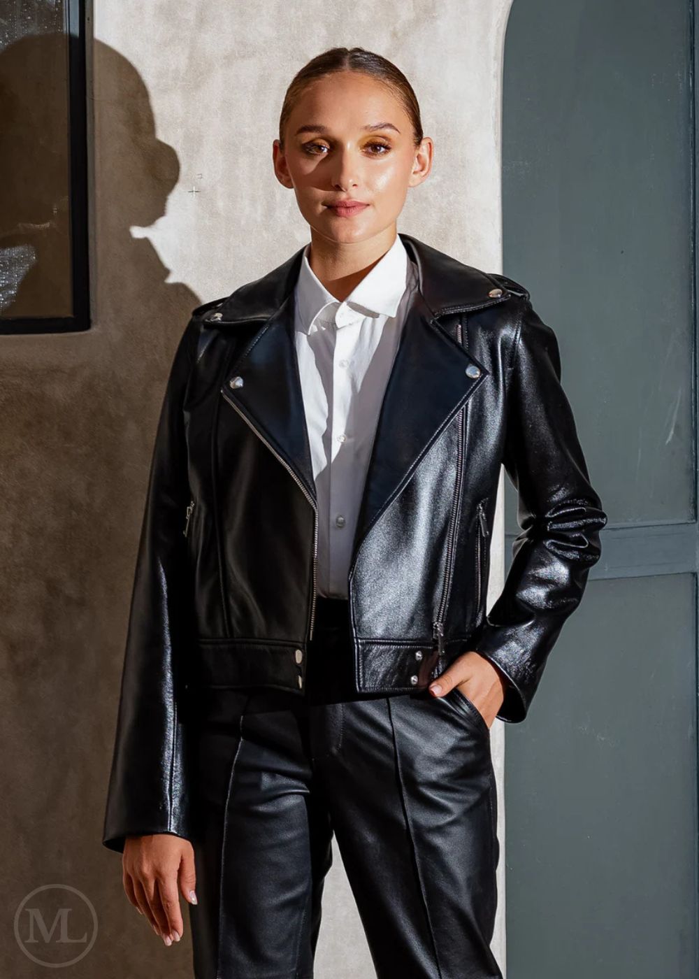 Women wearing a black leather biker jacket and pants against a neutral wall.