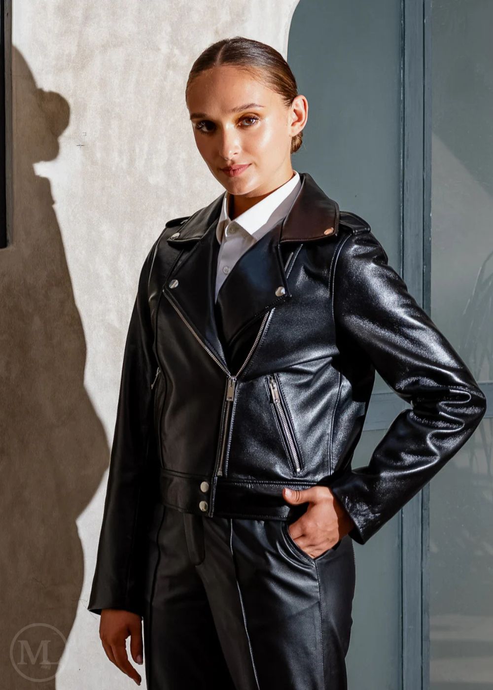 Women wearing a black leather biker jacket and pants against a neutral background