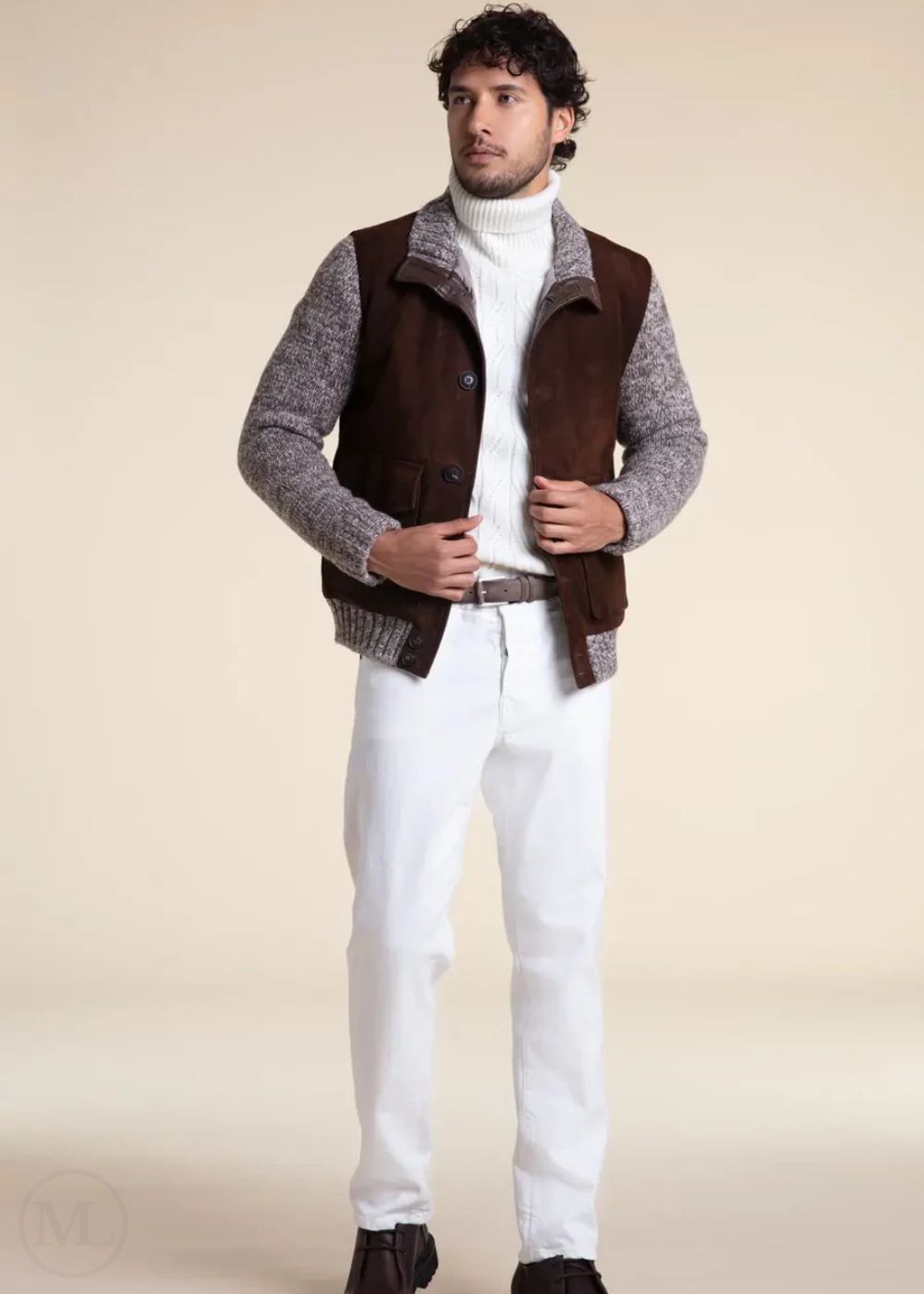 Man wearing a dark brown jacket over a gray sweater with white pants on a beige background