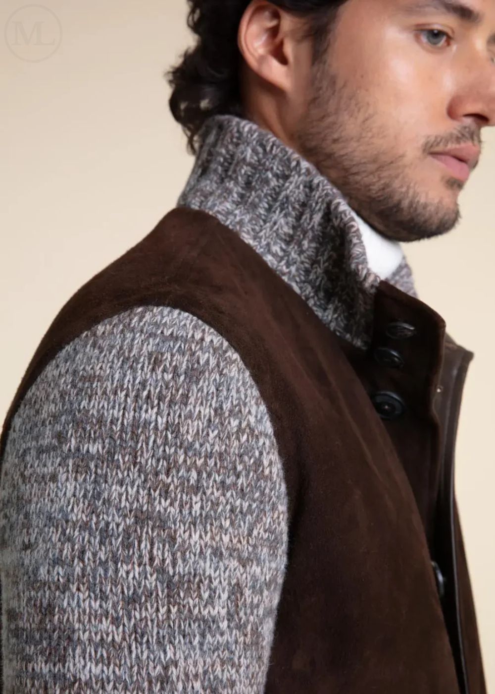 Man wearing a dark brown jacket over a gray sweater with a neutral background