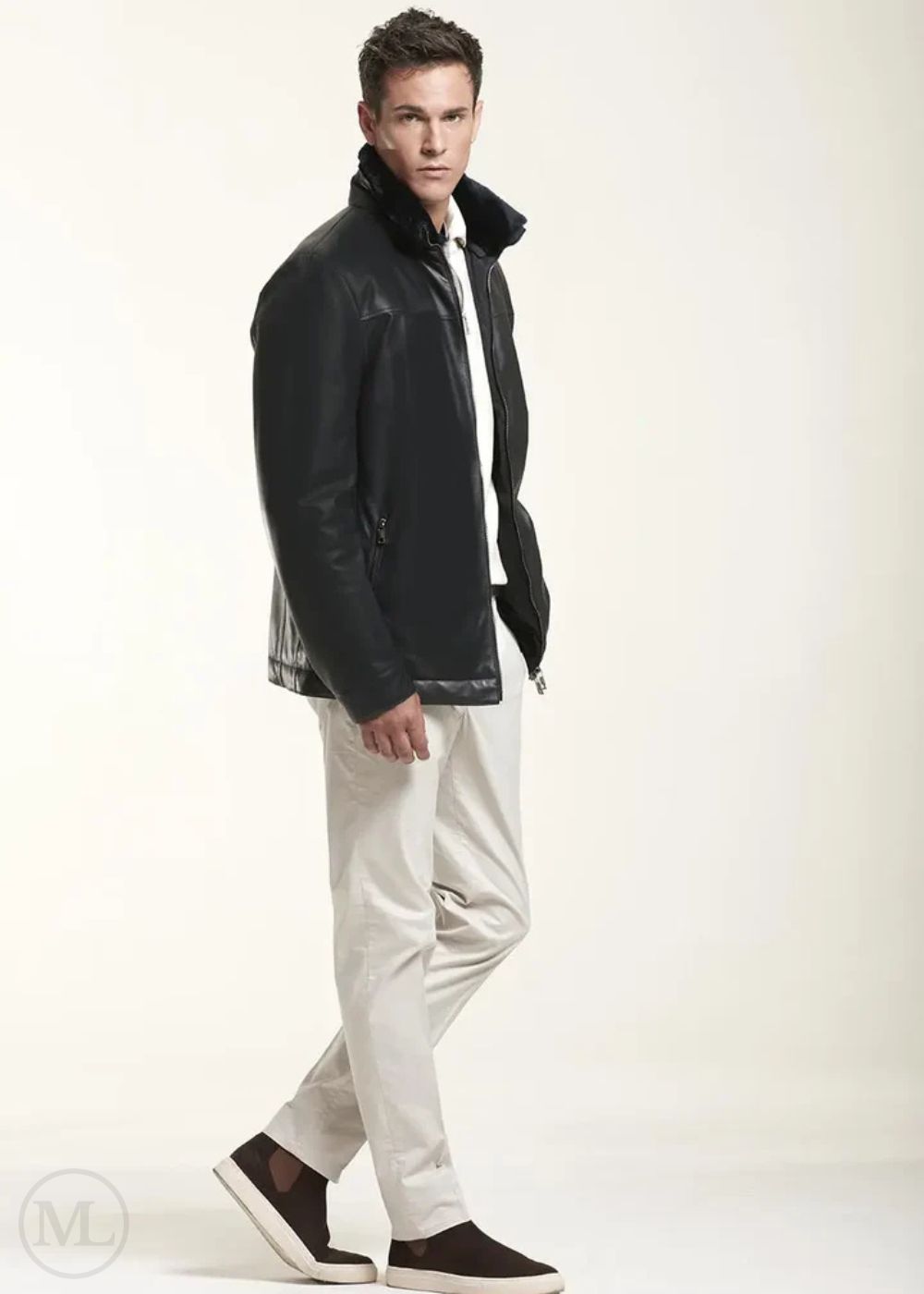 Man wearing a black leather jacket and white pants on a light background