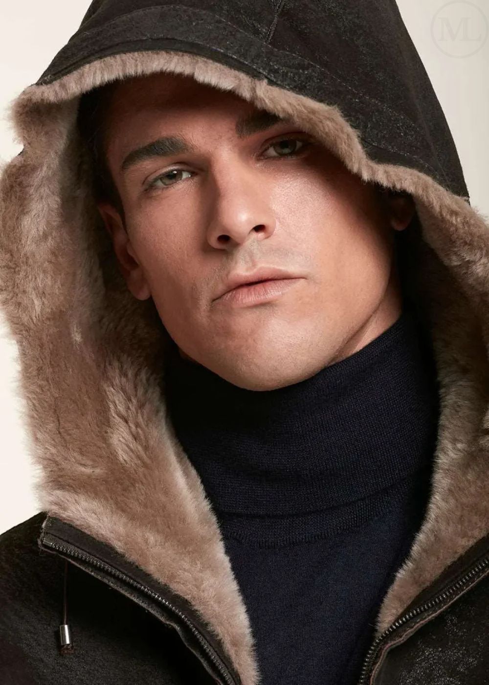 Man wearing a dark brown jacket with a fur-lined hood against a neutral background