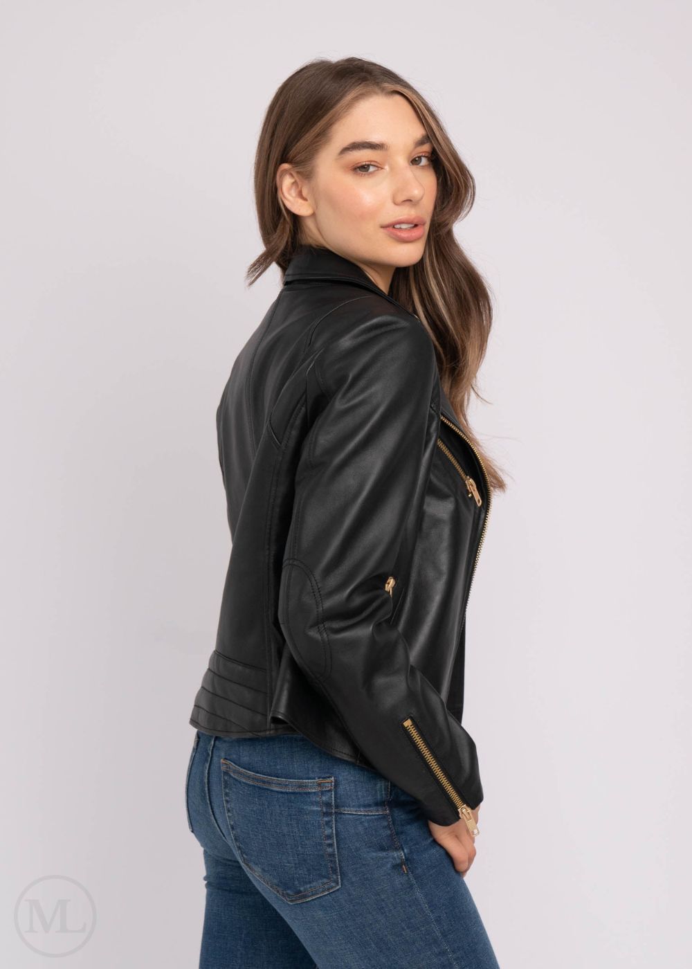 Femme portant une veste de motard en cuir noir et un jean bleu sur fond blanc