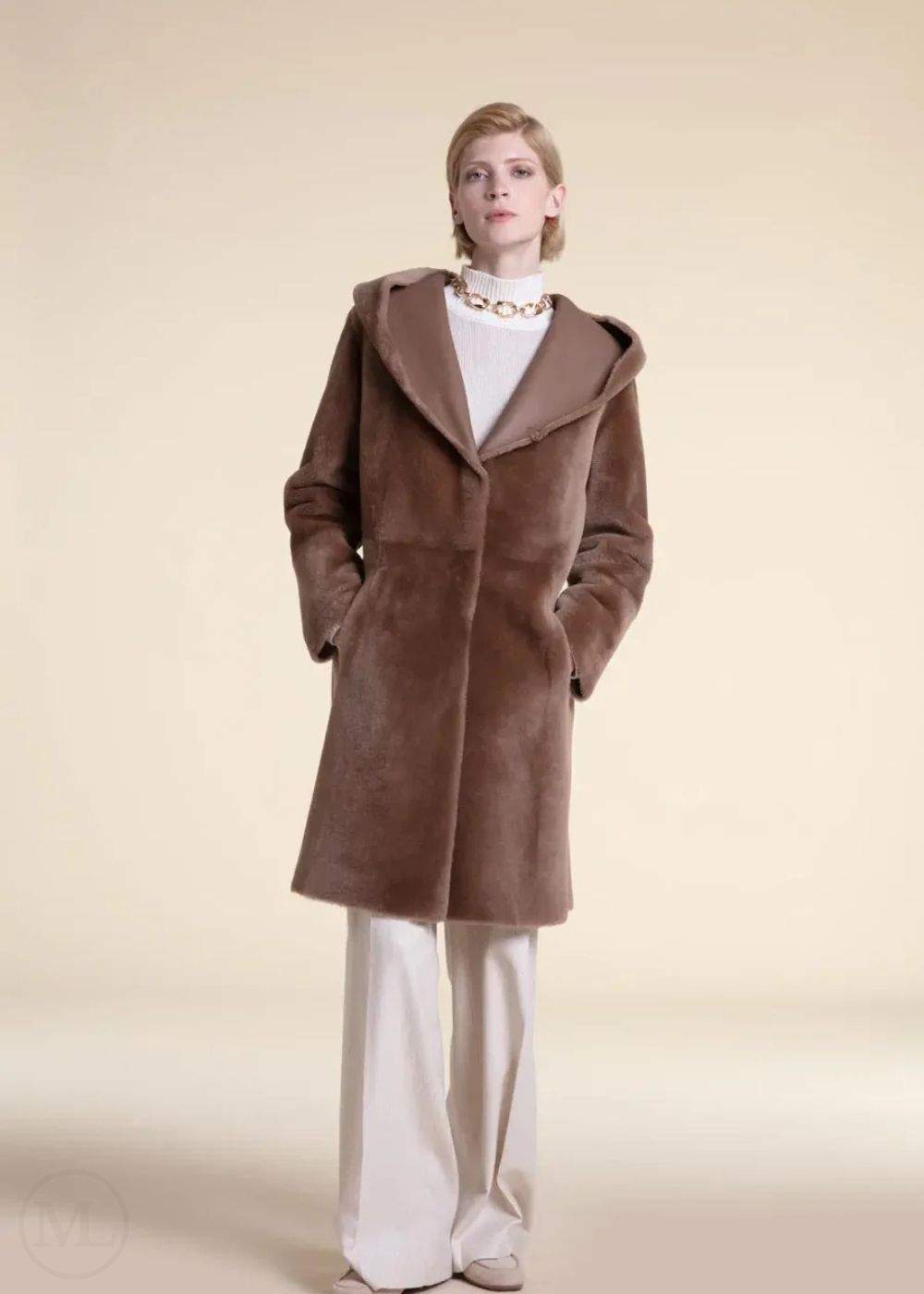 Woman wearing a beige shearling leather coat and white pants on a beige background