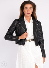 Woman wearing a black leather biker jacket over a white outfit on a plain background