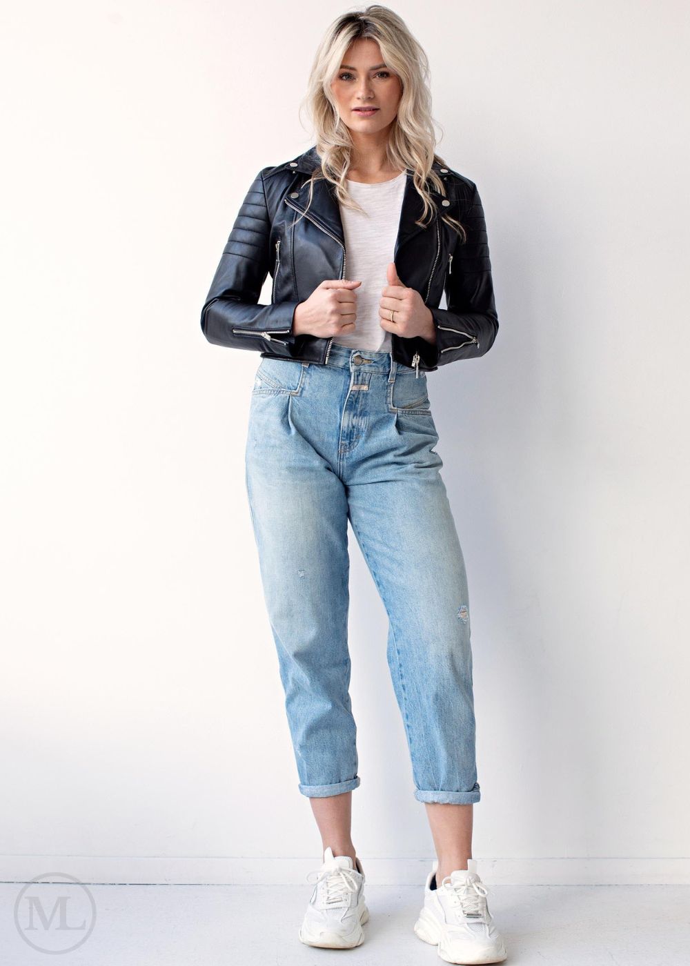 Women wearing a black leather biker jacket, white shirt, light blue jeans, and white sneakers on a white background