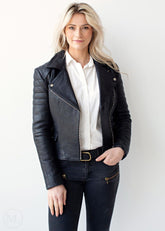 Woman wearing a black leather jacket over a white shirt and dark jeans on a white background