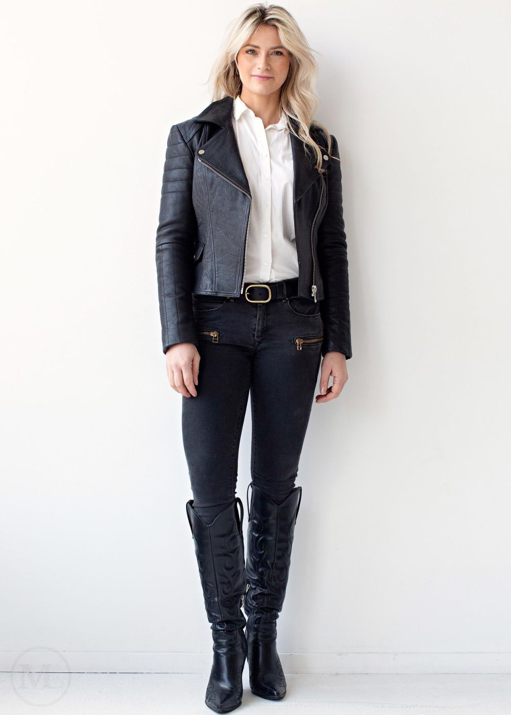 Woman wearing a black leather jacket, white shirt, black pants, and black knee-high boots against a white background.