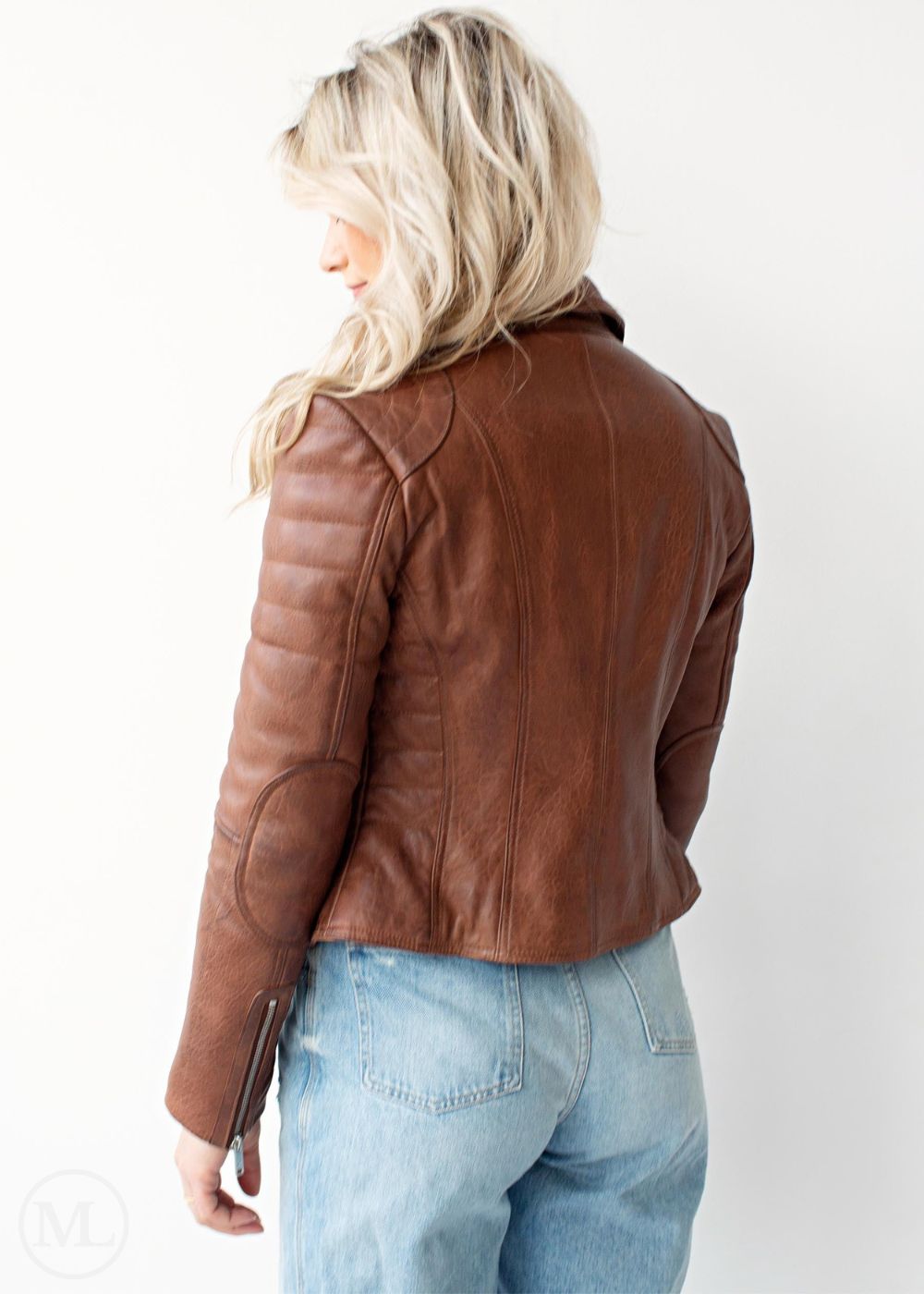 femme portant une veste en cuir marron cognac et un jean bleu sur fond blanc