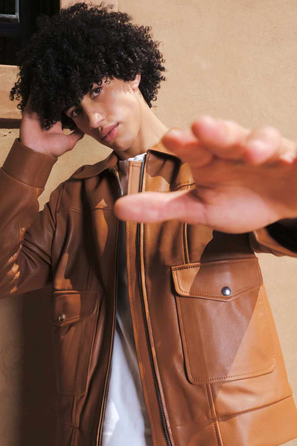 a young boy with curly hair giving a pose while wearing a Designer men’s camel color leather trucker jacket with flap chest pockets, and welt side pockets,