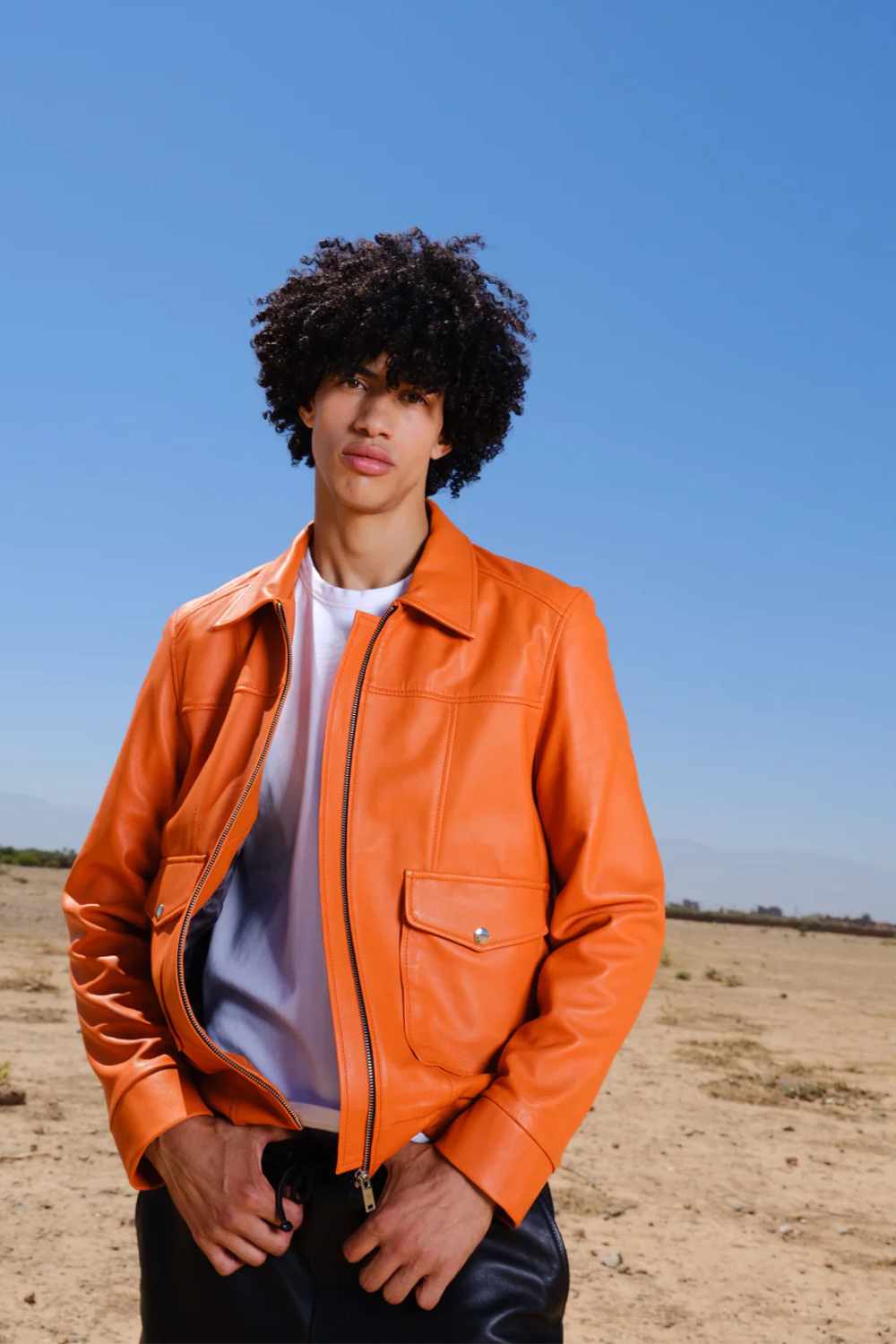 a young boy with curly hair wearing a Designer men’s leather trucker jacket with flap chest pockets, and welt side pockets in orange color