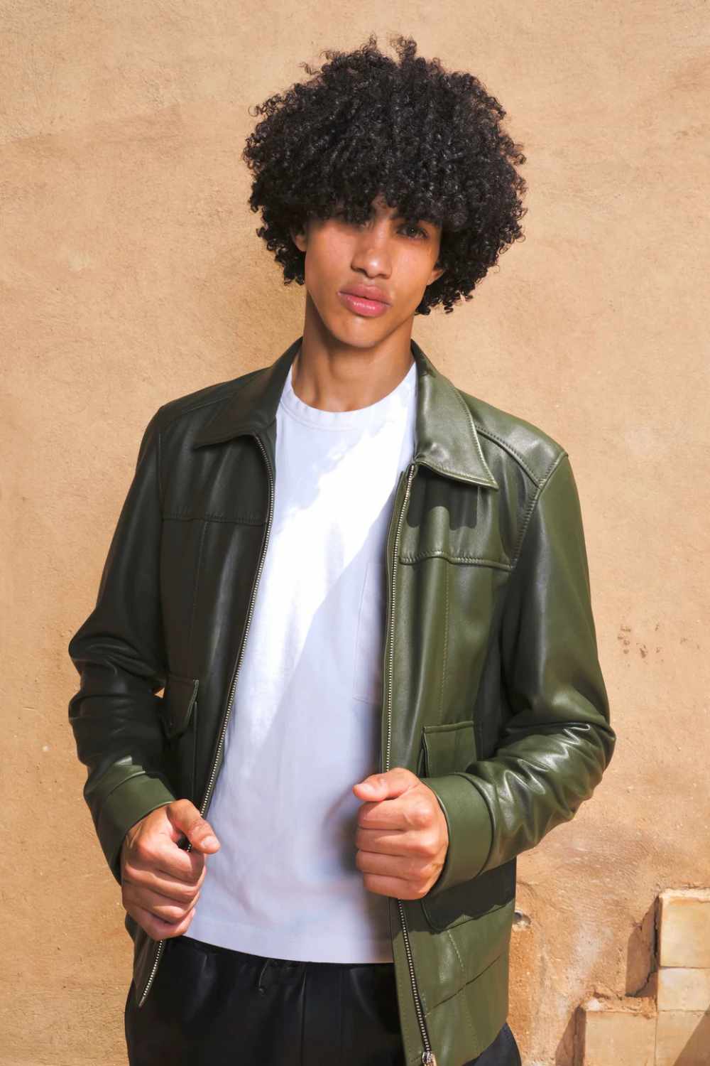 a young boy standing in beige bg wearing a Designer men’s khaki leather trucker jacket with flap chest pockets, and welt side pockets