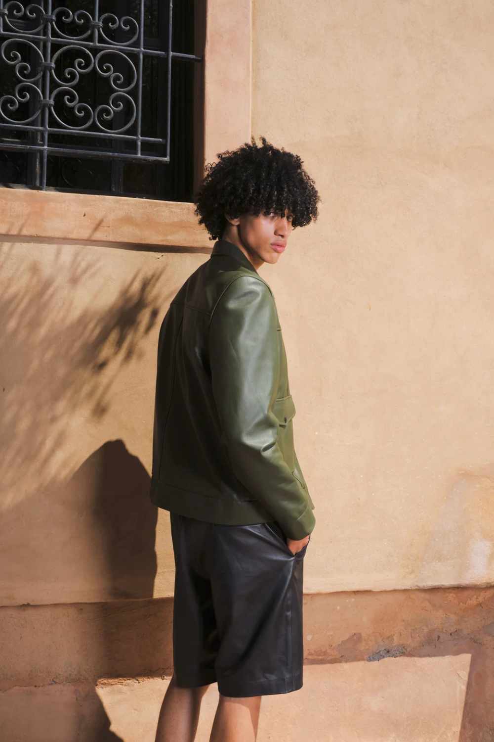 a young boy giving a side post, wearing a Designer men’s khaki leather trucker jacket with flap chest pockets, and welt side pockets, close shot