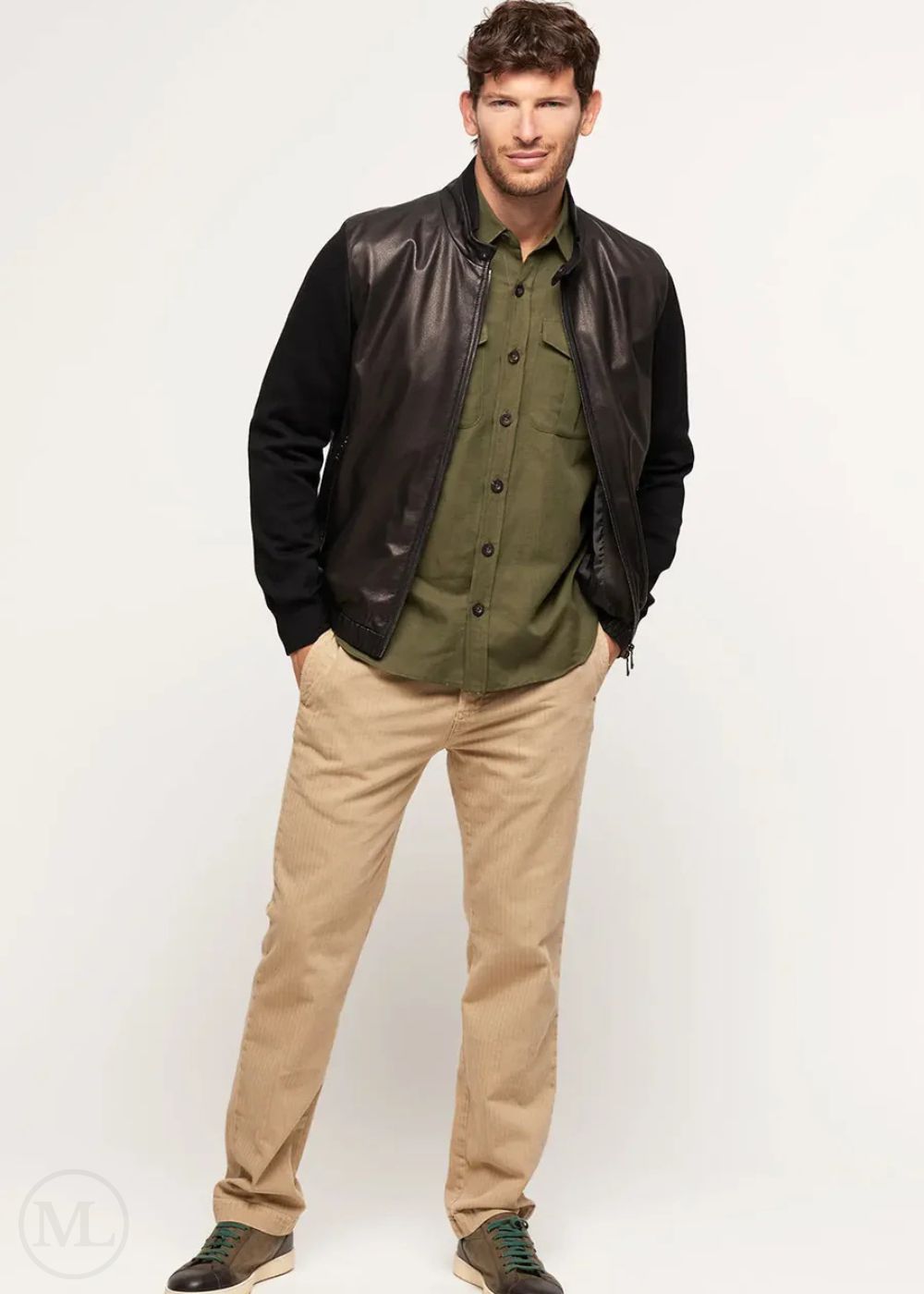 Man wearing a black leather bomber jacket over a green shirt and beige pants on a white background