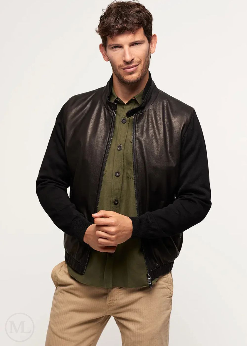 Man wearing a black leather bomber jacket over a green shirt and beige pants on a white background