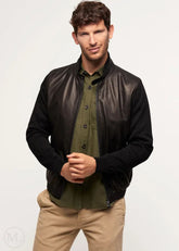 Man wearing a black leather bomber jacket over a green shirt and beige pants on a white background