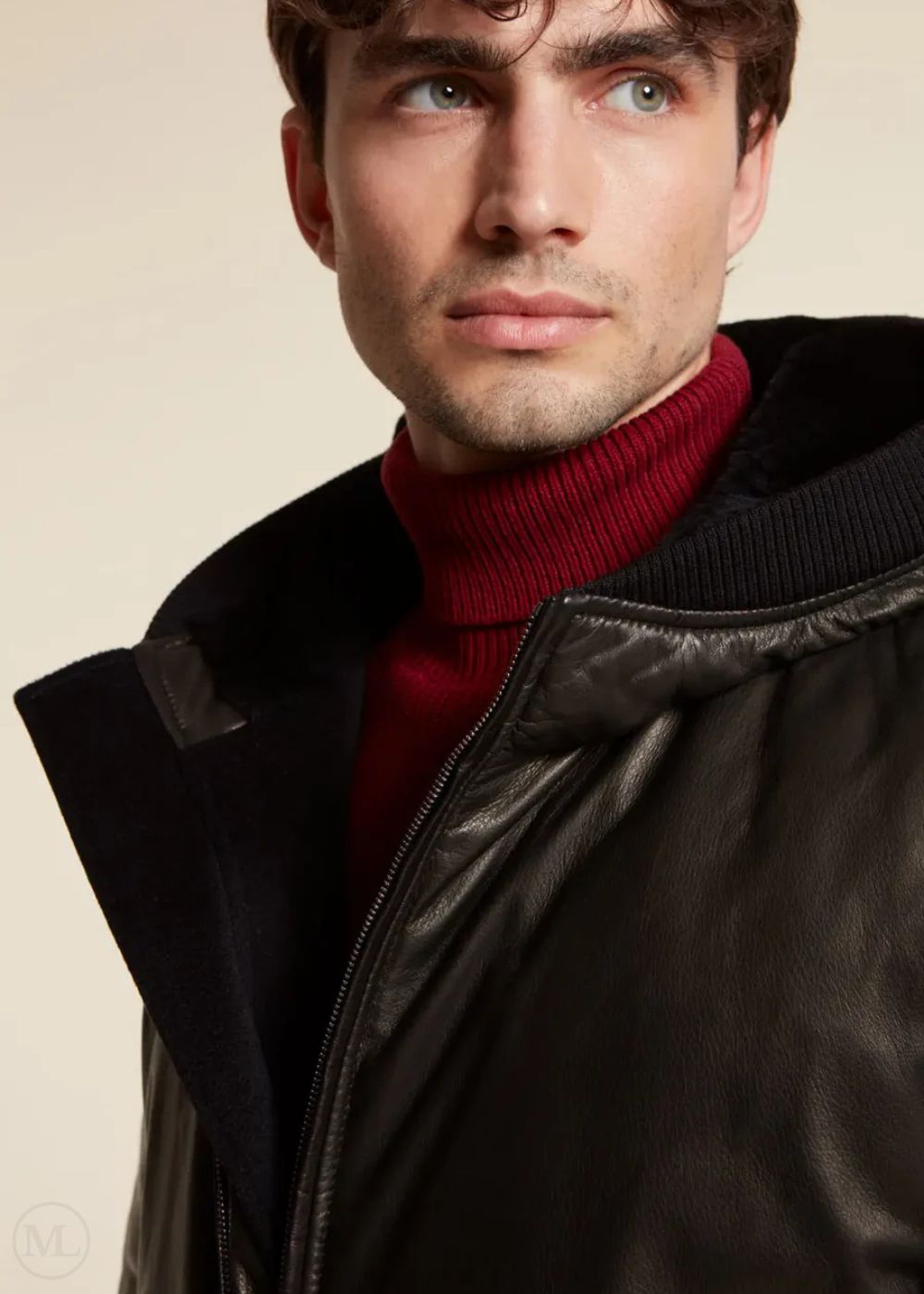 Man wearing a black leather jacket over a red sweater against a beige background