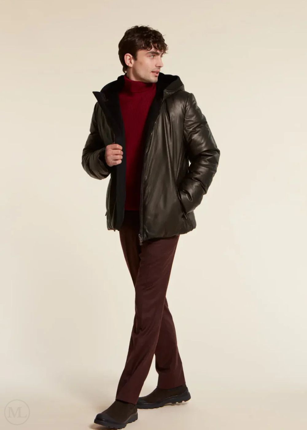 Man wearing a black leather jacket over a red sweater on a beige background