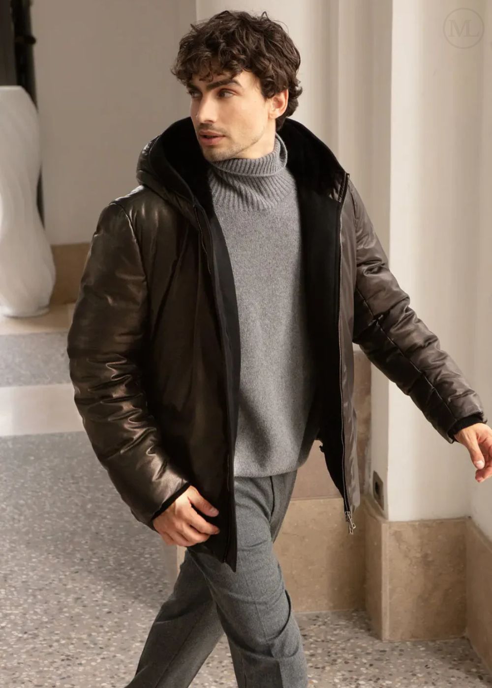 Man wearing a black leather jacket with fur lining in an indoor setting.