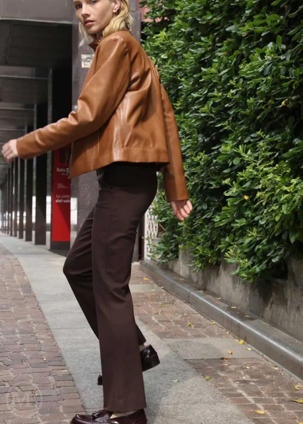 Women wearing a brown leather Moto jacket and dark pants walking on a sidewalk.