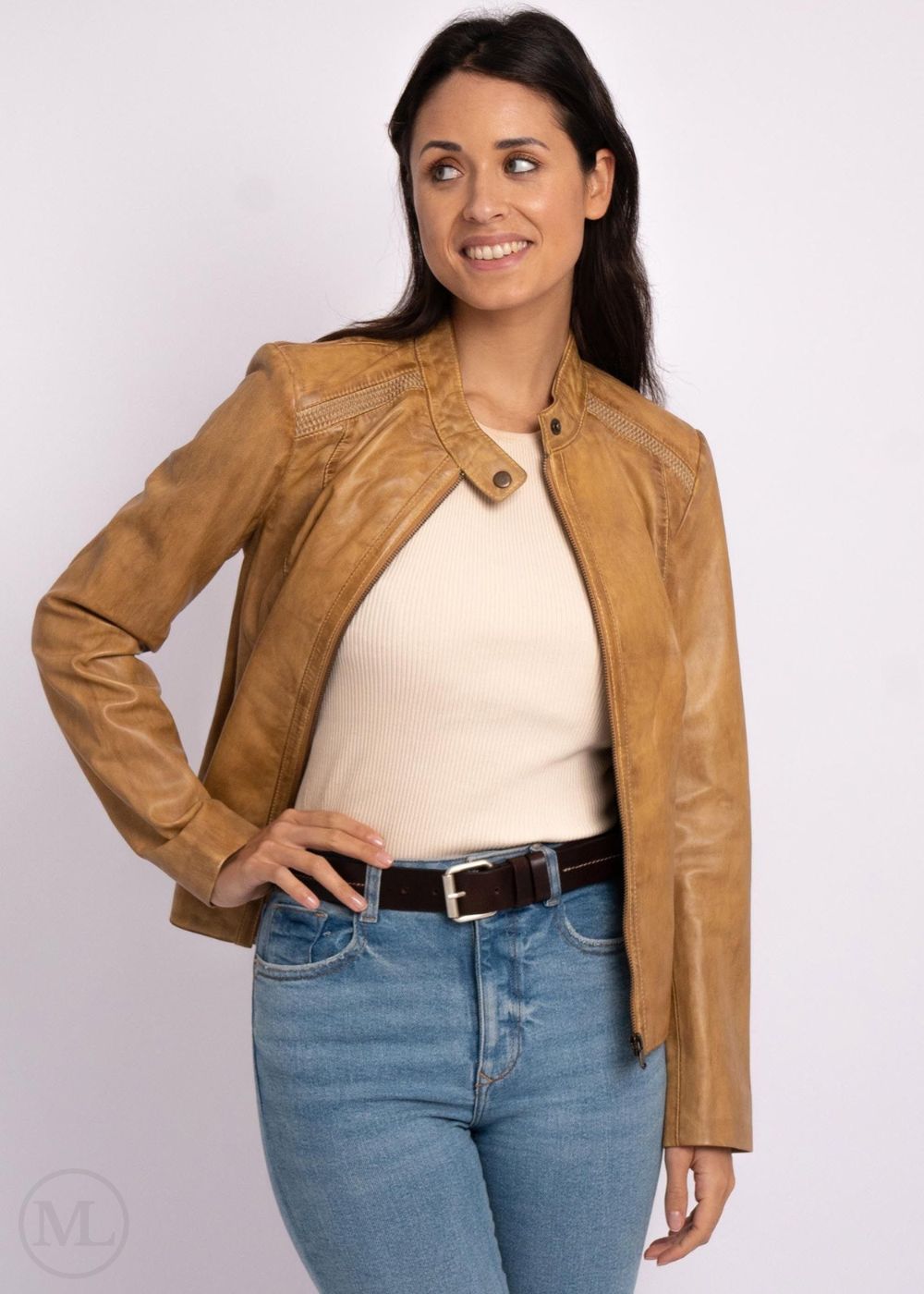 Woman wearing a camel leather biker jacket, white top, and blue jeans on a white background