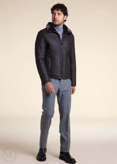 Man wearing a dark grey leather aviator jacket and gray pants on a beige background