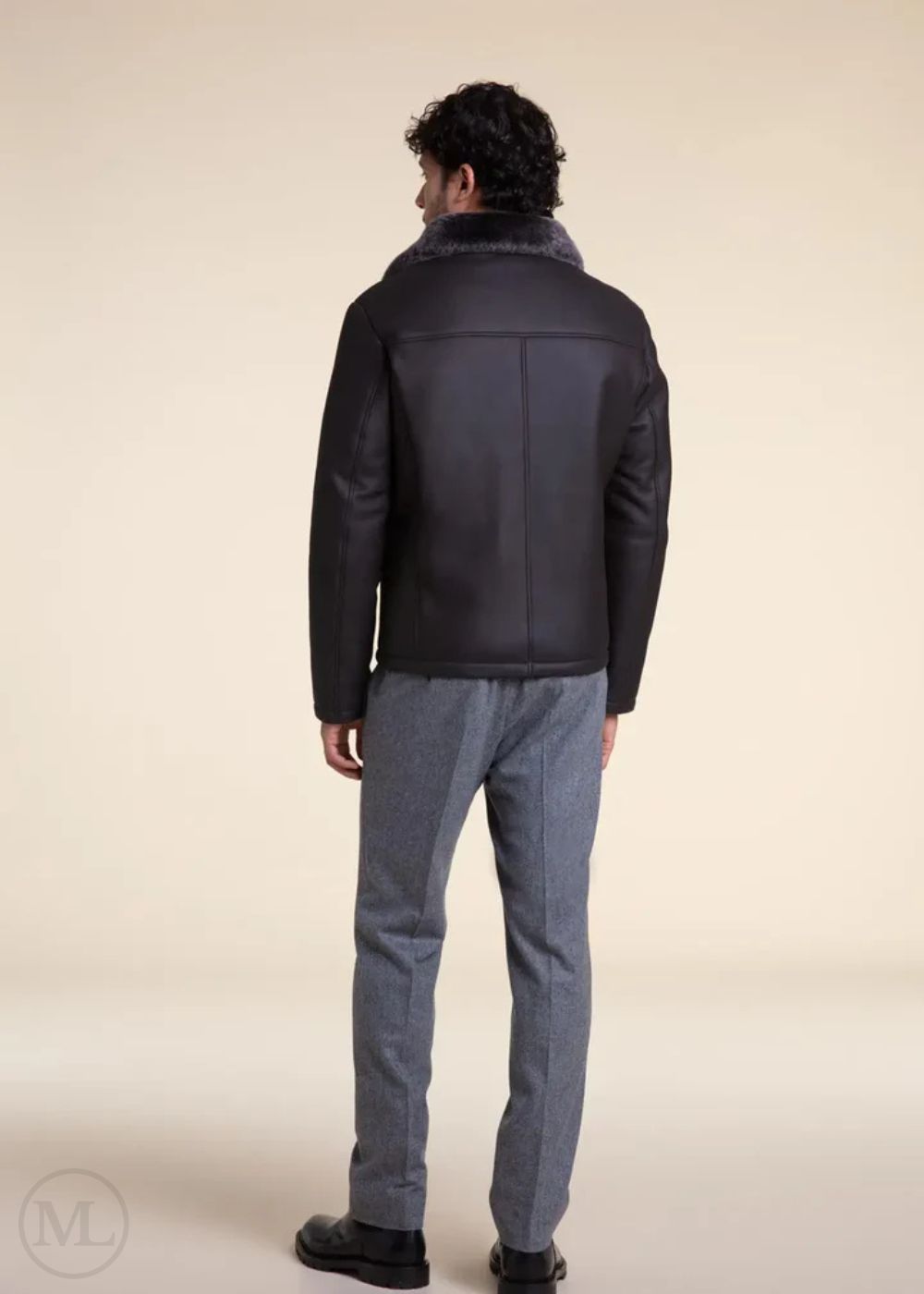 Man wearing a dark grey aviator leather jacket and gray pants on a beige background