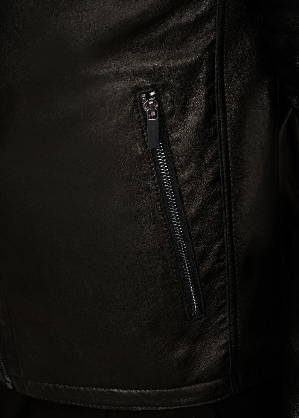 Close-up of a black leather biker jacket with a zipper detail on a dark background