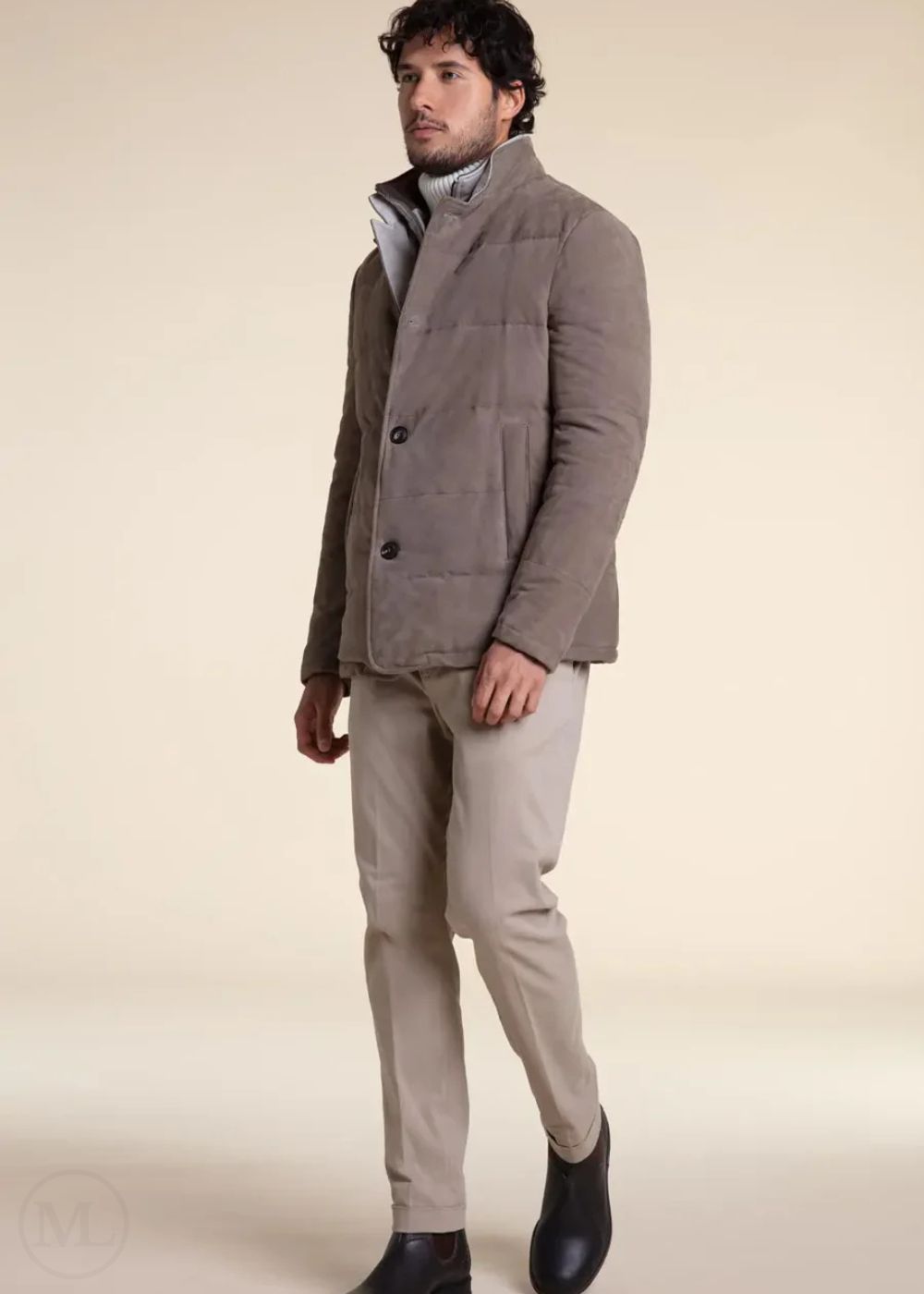 Man wearing a camel suede leather jacket and beige pants on a plain background