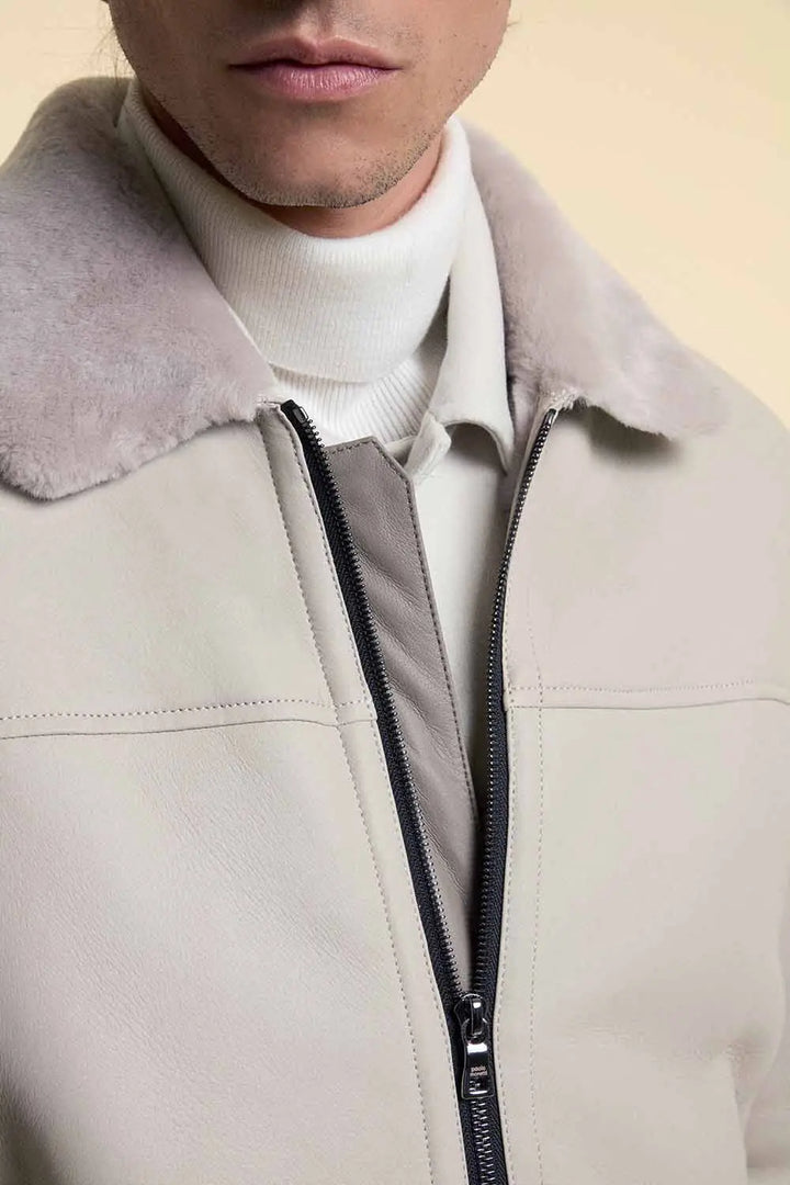 Close-up of a white shearling leather jacket with a zipper and white shirt underneath on a beige background