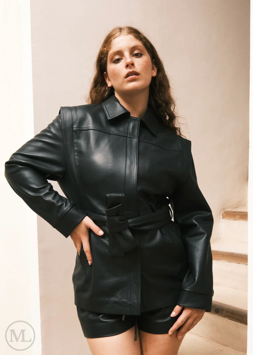Woman wearing a black leather Coat outfit against a neutral background