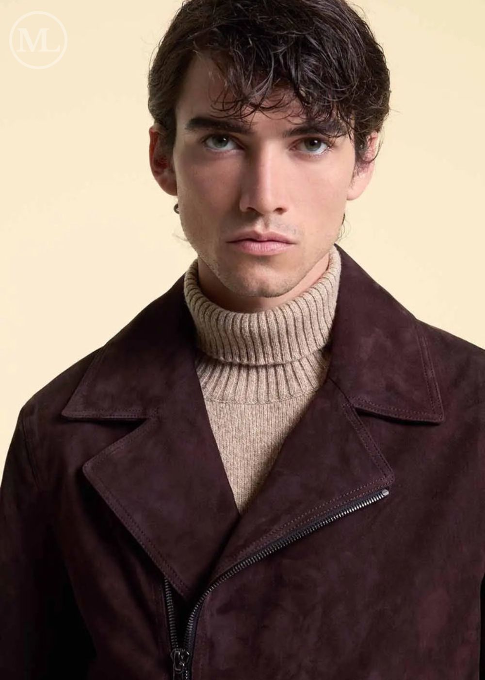 Man wearing a dark brown suede jacket over a beige turtleneck sweater on a beige background