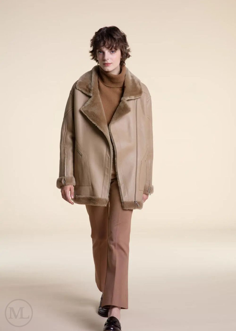 Women wearing a camel shearling leather coat with fur collar on a plain background