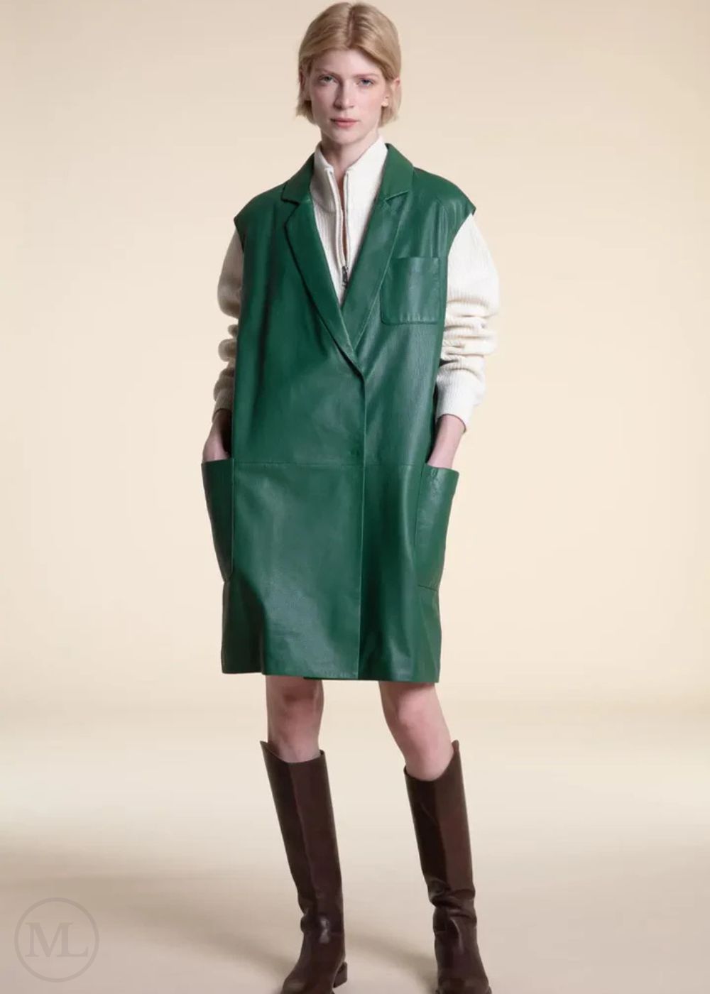 Woman wearing a green leather dress over a white shirt with brown knee-high boots on a beige background